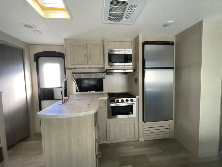Bright RV rental kitchen features light cabinets, a sink, stove, microwave, and refrigerator, ideal for comfortable travel.. Coachmen Catalina 2022