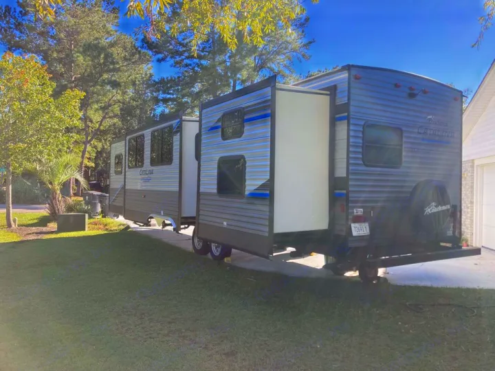 This large Catalina travel trailer, an RV rental, is parked with slide-outs open in a grassy yard.. Coachmen Catalina 2022