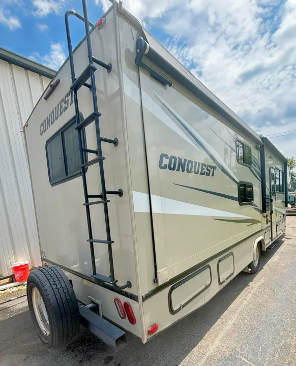 Side and rear view of a "CONQUEST" motorhome/RV, featuring a ladder, spare tire, and awning. Great for rv rental trips.. Gulf Stream Conquest 2020