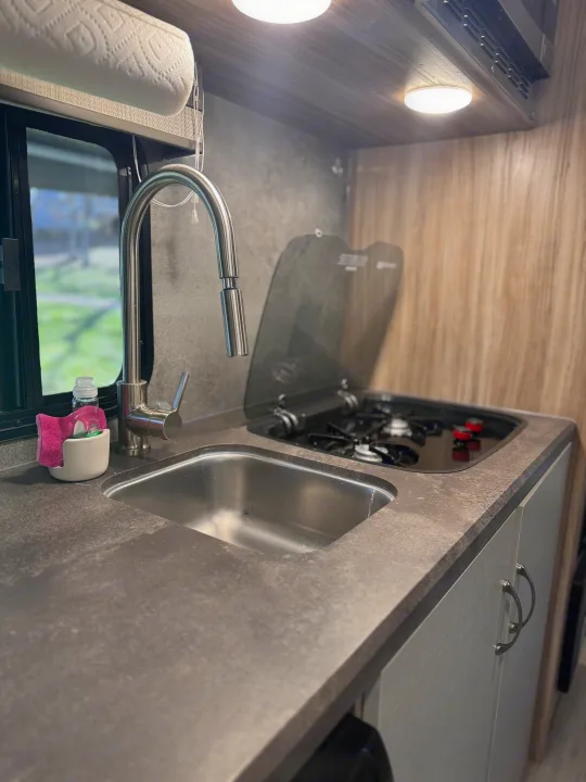 This RV rental kitchen offers a sleek sink, pull-down faucet, and two-burner stovetop on a modern countertop, ideal for cooking on the road.. Winnebago Minnie Winnie 2022