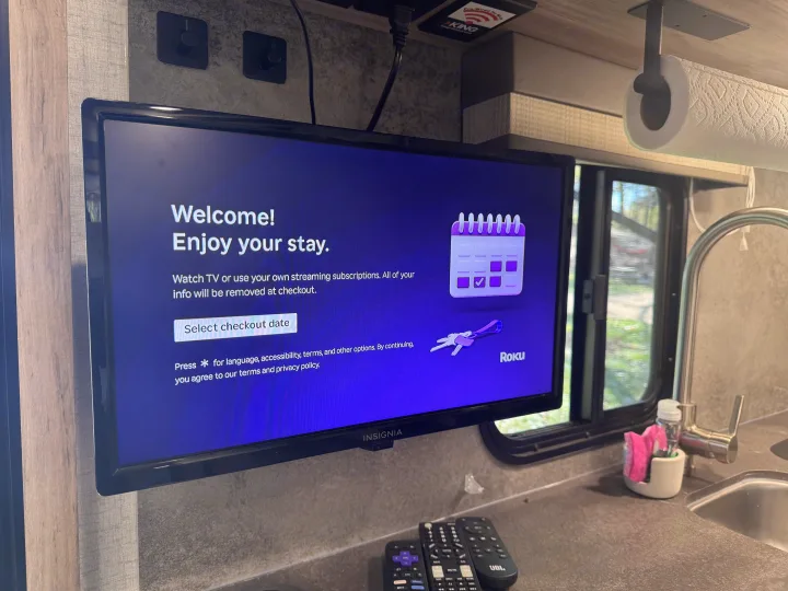 This RV rental features a mounted Insignia TV displaying a Roku welcome screen, with remotes, a sink, and paper towel holder nearby.. Winnebago Minnie Winnie 2022