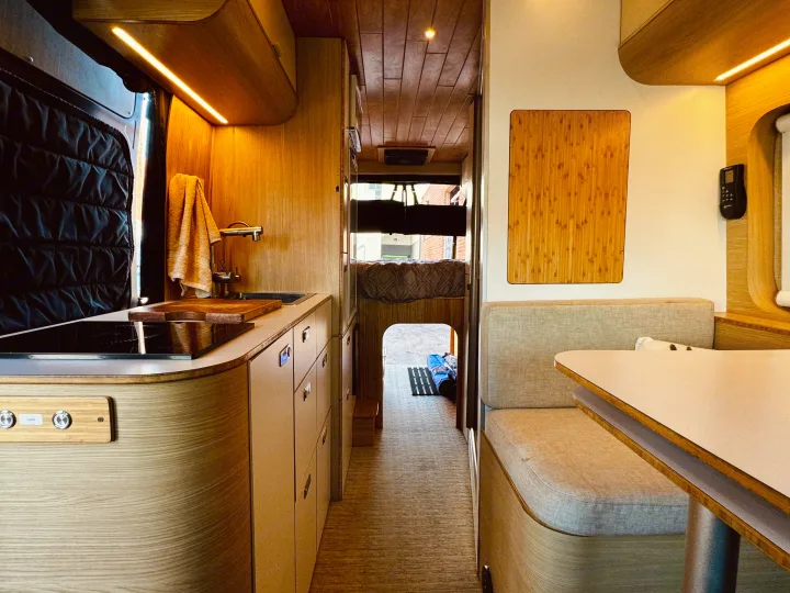 Cozy rv rental interior featuring a compact kitchen, dinette, and bed. Warm wood finishes and efficient design for travel.. Noovo Lite 2023