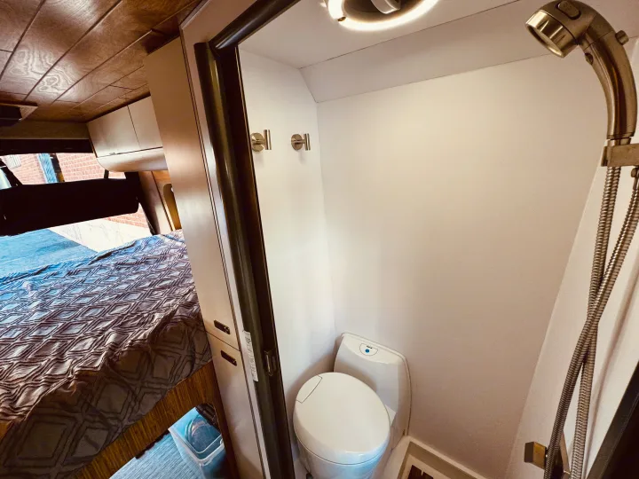 Cozy RV rental interior showcasing a patterned bed, and a compact wet bath with a modern toilet and shower.. Noovo Lite 2023