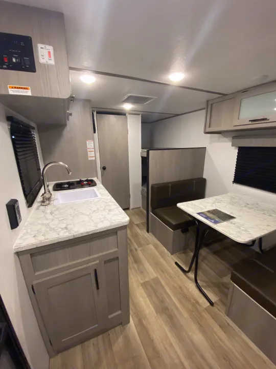 RV rental interior: a bright, compact space with kitchen, dining booth, and bunk beds, featuring modern finishes.. Coleman Lantern 17B 2024