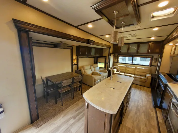 Spacious RV rental interior featuring a kitchen island, dining area with table and chairs, and comfortable living space with recliners.. Grand Design Solitude 2019