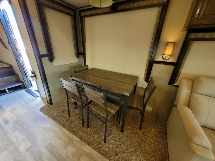 Bright RV rental interior: wood-look dining table, 4 chairs, and a light-colored sofa on plush carpet.. Grand Design Solitude 2019
