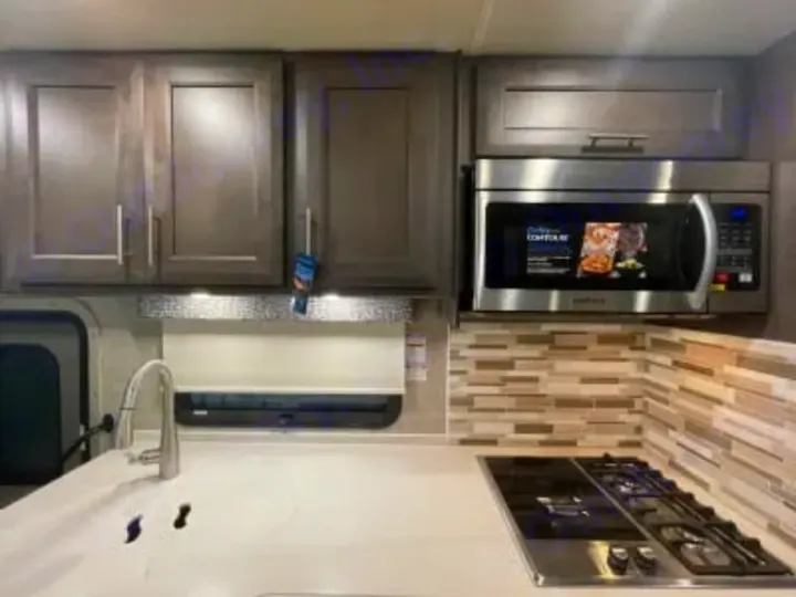 RV rental kitchen area: Features modern gray cabinets, stainless microwave, gas cooktop, sink, and tiled backsplash.. Thor Miramar 2022