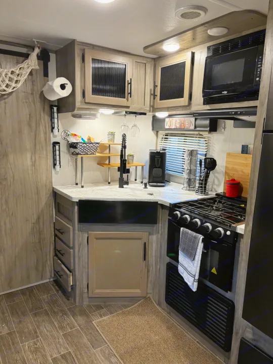 Clean and modern RV rental kitchen with wood-look cabinetry, microwave, stove, sink, and smart storage solutions.. Forest River Cherokee Alpha Wolf 2022
