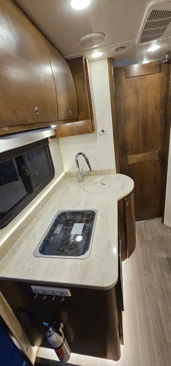 Clean RV rental kitchen interior: wood cabinets, light counter, sink, covered stove, and ambient lighting.. Wayfarer Wayfarer Motorhome 2018