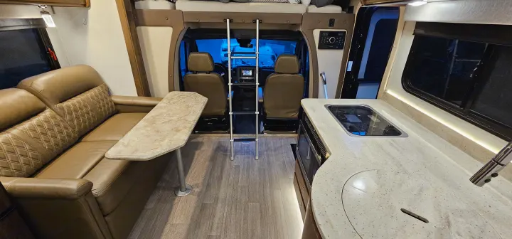 This RV rental interior offers a comfortable living area with a leather couch, a full kitchen, and an overhead bunk with ladder.. Wayfarer Wayfarer Motorhome 2018