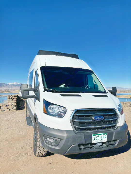 Scenic Colorado adventure with a white Ford Transit RV rental, parked by a lake with snow-capped mountains.. Ford Ford Transit 2020