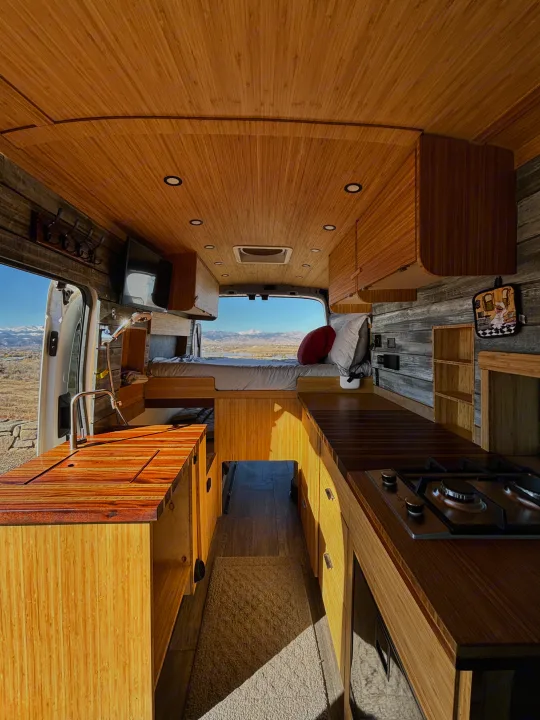 Cozy camper van interior with bamboo finishes, kitchenette, bed, and a scenic mountain view, perfect for your next rv rental adventure.. Ford Ford Transit 2020