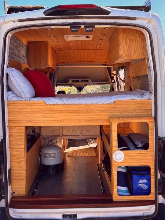 RV rental: Inside a modern camper van, featuring an elevated bed, bamboo wood interior, and functional under-bed storage.. Ford Ford Transit 2020