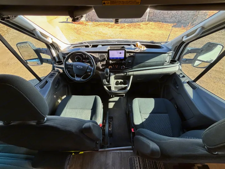 RV rental interior: View of a Ford van's cockpit from the rear, showing the dashboard, steering wheel, and front seats.. Ford Ford Transit 2020
