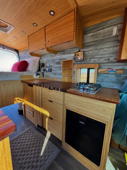 Inside an RV rental: a modern bamboo interior with kitchen, stove, fridge, and cozy bed. Wood paneling & natural light.. Ford Ford Transit 2020