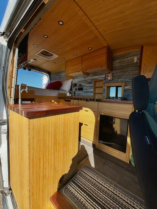 Step inside this custom bamboo RV rental, featuring a cozy bed, modern kitchen, and sleek wood interior for your next adventure.. Ford Ford Transit 2020