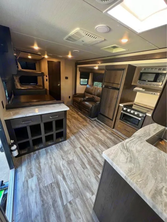 Modern RV rental interior featuring kitchen, recliners, and bunk beds on light wood-look flooring.. Grand Design Transcend Xplor 2021