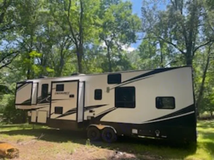 This large white and black fifth-wheel RV rental is parked in a treed setting, perfect for travel and camping adventures.. Dutchmen 3586 2019