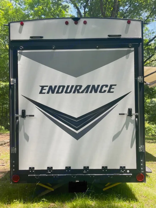 Rear view of a white Endurance toy hauler RV rental. Features include a large ramp door, taillights, and a camera mounted above.. Dutchmen 3586 2019