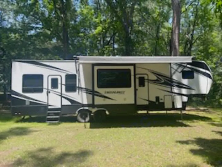 This white fifth-wheel RV rental, with awning out, is set up at a green campsite. Perfect for your next trip!. Dutchmen 3586 2019