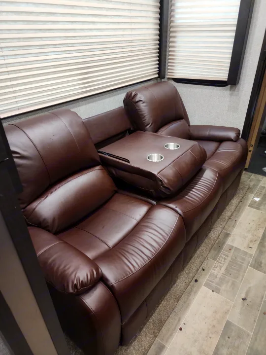 RV rental interior: cozy brown leather reclining sofa with center console and blinds for comfort.. Dutchmen 3586 2019