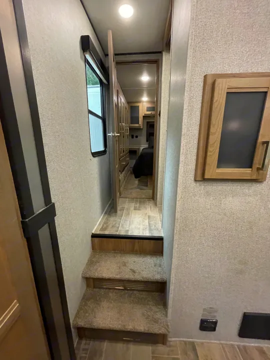 View of an RV rental's interior, featuring carpeted stairs leading to a hallway and bedroom area with cabinets.. Dutchmen 3586 2019