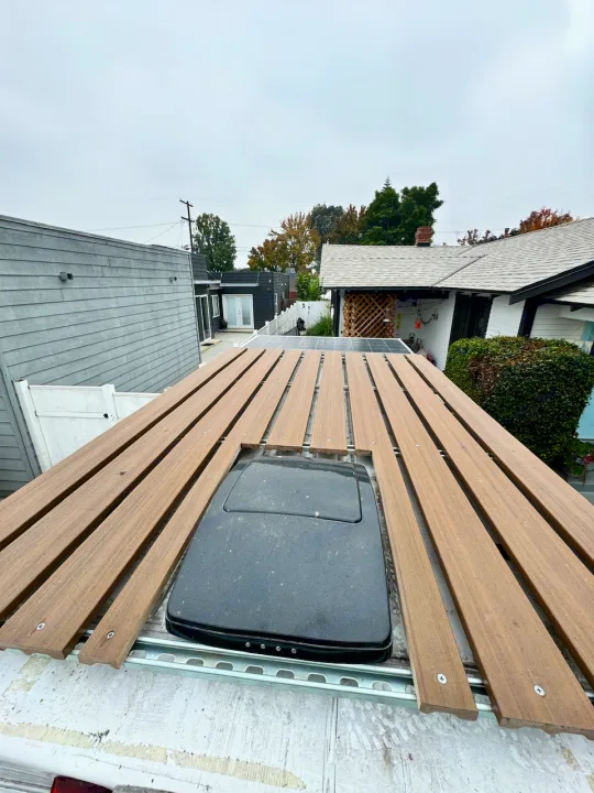 Overhead view of an RV rental's custom rooftop deck. Wooden slats surround a black roof vent, enhancing outdoor space.. Dodge Ram 1500 2020