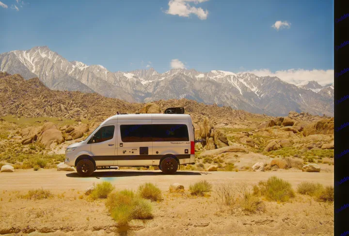 This silver RV rental van is perfectly suited for adventure, parked in a rocky desert with majestic snow-capped mountains.. Thor Tranquility 2023