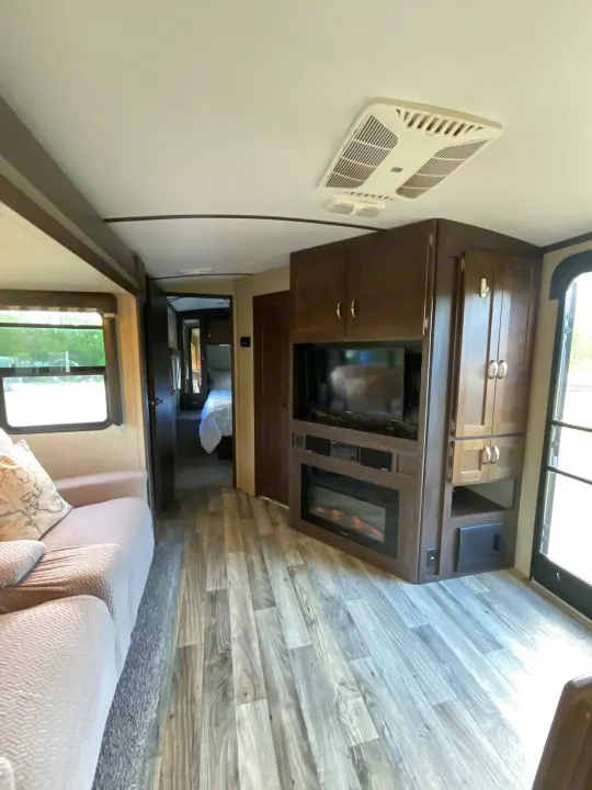 Spacious RV rental interior with modern living area, TV, electric fireplace, and bedroom visible beyond the hallway.. Keystone RV Outback Super-Lite 2018