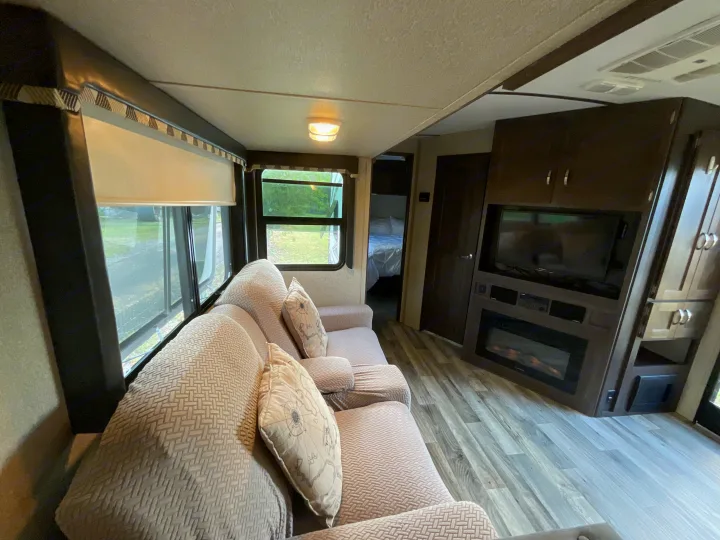 Inside a modern RV rental: inviting living area with a large sofa, TV, fireplace, and bedroom beyond. Cozy travel trailer space.. Keystone RV Outback Super-Lite 2018