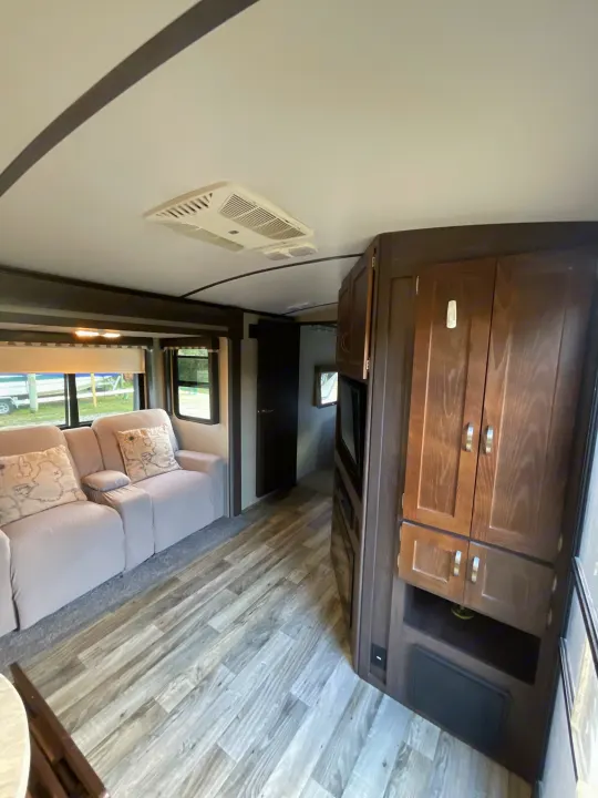 RV rental interior: Comfortable living space with light-colored recliners, modern wood-look floor, dark cabinets, and ceiling AC.. Keystone RV Outback Super-Lite 2018