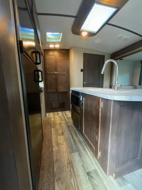 Bright RV rental interior, highlighting a modern kitchen island with sink and microwave, plus fridge and wood-look flooring.. Keystone RV Outback Super-Lite 2018