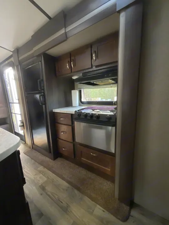 RV rental kitchen: Black fridge, stove/oven, wood cabinets, and practical flooring. A small rug is visible near the entrance. Compact interior.. Keystone RV Outback Super-Lite 2018
