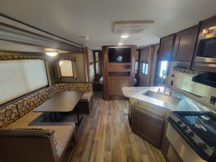 RV rental interior with a kitchen, dining booth, living area, and glimpse of a sleeping space.. Keystone RV Hideout LHS 2019