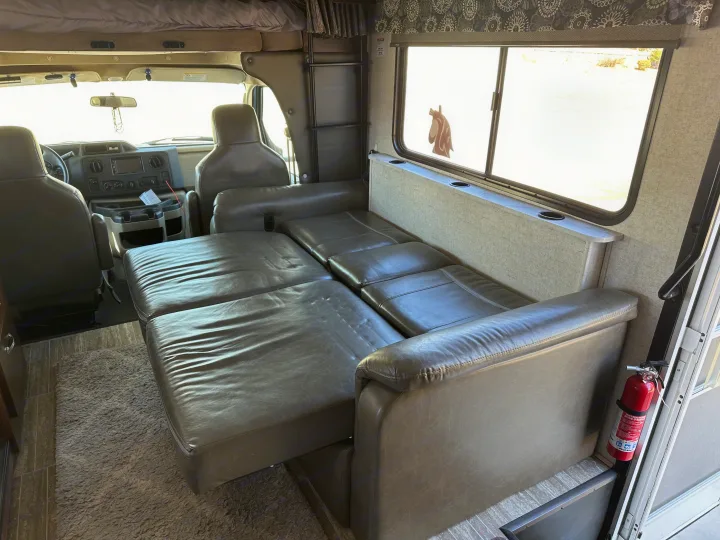 Inside an RV rental: a plush, extended sofa bed provides comfortable sleeping near the cockpit and a large window.. Forest River Sunseeker 2018