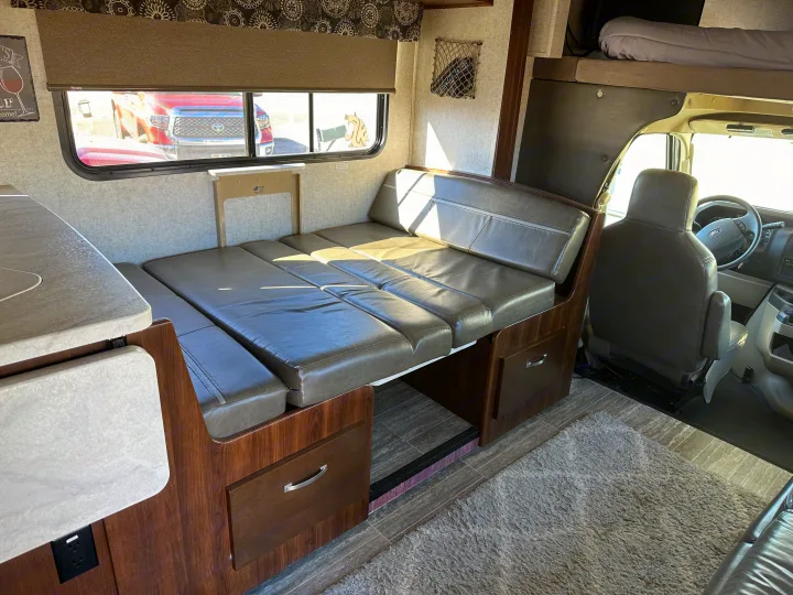 RV rental interior featuring a dinette converting into a bed, an overhead bunk, and the driver's cab visible.. Forest River Sunseeker 2018