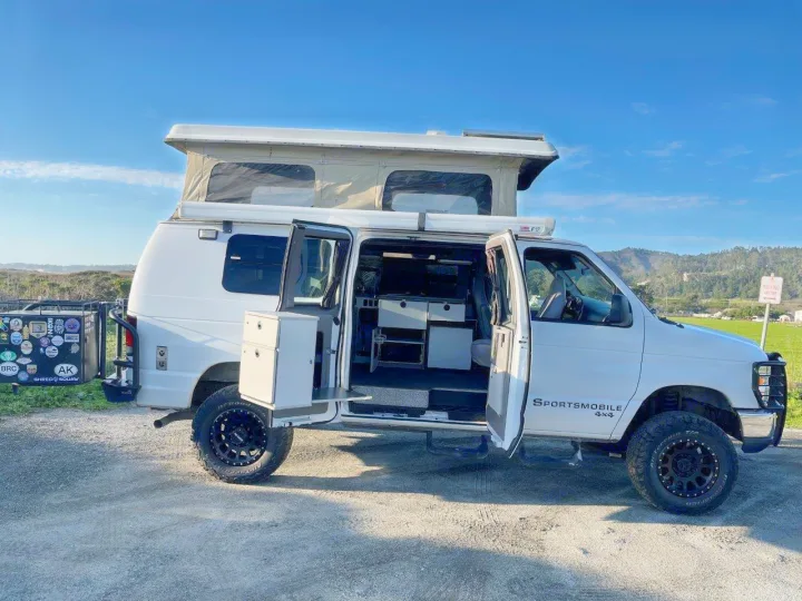 Explore in a white 4x4 pop-top camper van, doors open revealing the interior. Your ultimate rv rental adventure awaits!. Ford E250 2008