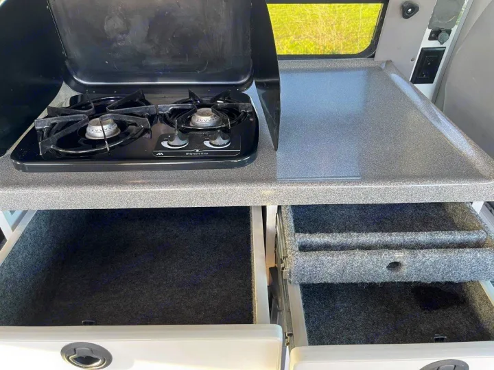 RV rental kitchen with a two-burner stove, counter, and felt-lined storage drawers, ready for your next adventure.. Ford E250 2008