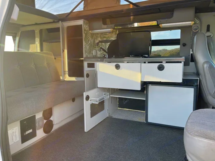 Explore the comfortable interior of this RV rental camper van, featuring a built-in kitchen, bed, and storage.. Ford E250 2008