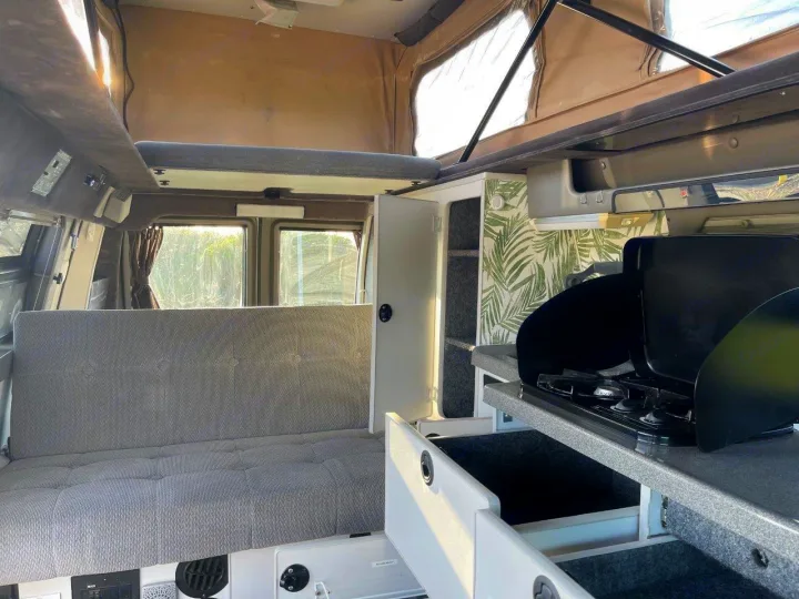 Inside an RV rental: view of the gray upholstered seating/bed area, kitchen with stove, and pop-top ceiling. Ready for adventure.. Ford E250 2008