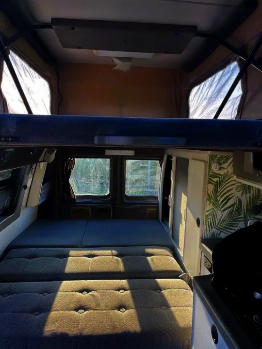 View inside an RV rental pop-top camper, showing a lower convertible bed, upper loft bed, and a compact kitchen.. Ford E250 2008