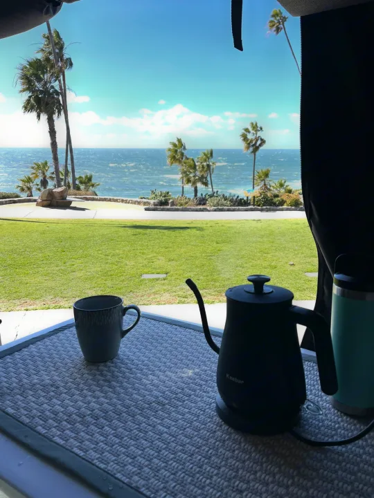 Scenic rv rental view: ocean, palm trees, and morning coffee brewing with a Keebar kettle. Relaxing travel.. Storyteller Overland Storyteller Overland Class B 2023