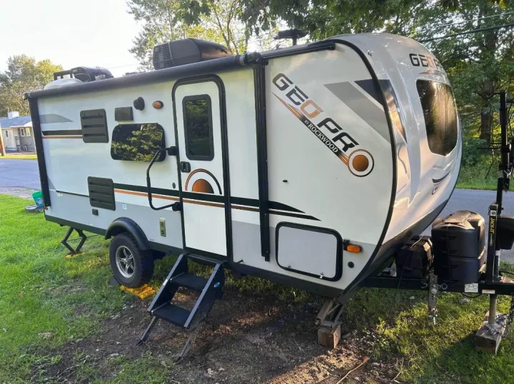This white Geo Pro travel trailer, an ideal RV rental, is set up with steps & leveling jacks on grass.. Forest River Rockwood Geo Pro 2022