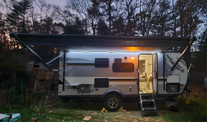 An inviting RV rental shines under its LED-lit awning at dusk, showing a comfy interior ready for adventure.. Forest River Rockwood Geo Pro 2022