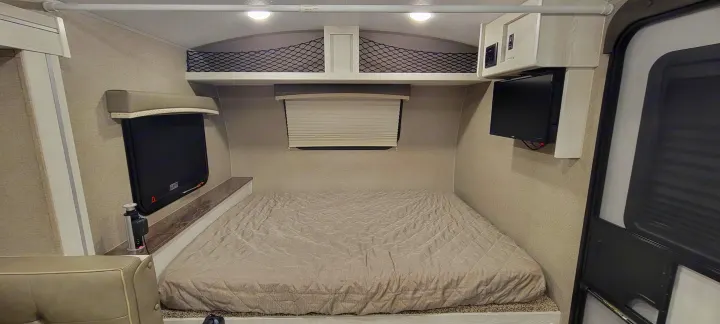 Cozy RV rental bedroom with a quilted bed, windows, mounted TV, pop-up outlet, and overhead storage.. Forest River Rockwood Geo Pro 2022