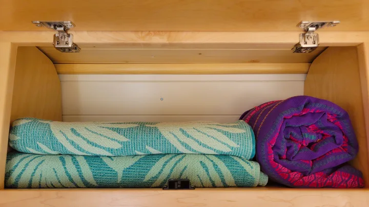 RV rental storage: Light wood cabinet with rolled colorful blankets, door hinges, and a magnetic latch.. Mercedes-Benz Sprinter 2021