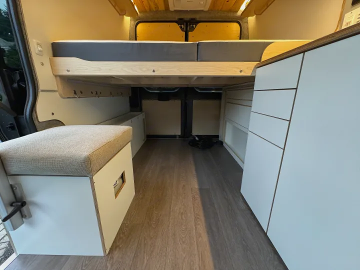 Spacious RV rental interior with a cozy bed, bench seating, white cabinetry, and wood flooring.. Dave & Matt Vans Dave & Matt Vans Class B 2024