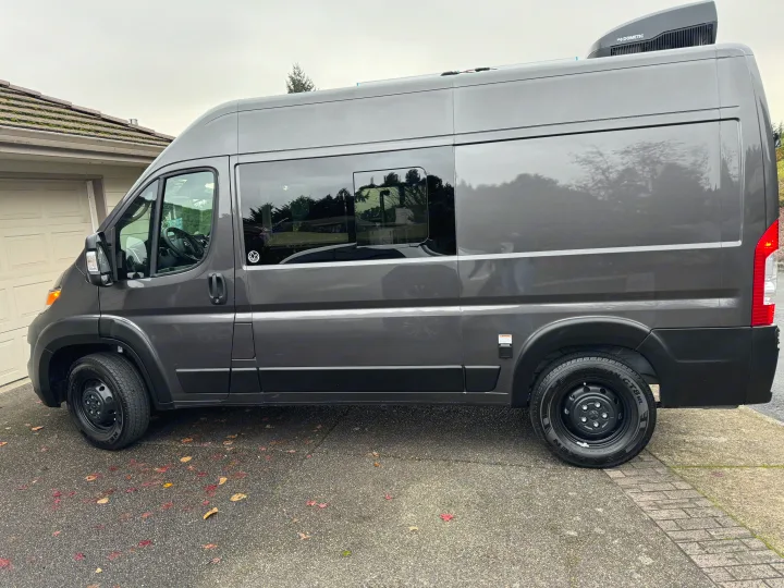 Sleek gray camper van, ideal for RV rental. Side view with windows, roof AC unit, and external electrical connection.. Dave & Matt Vans Dave & Matt Vans Class B 2024