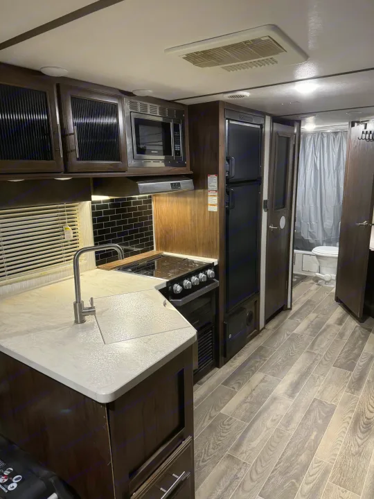 Modern RV rental interior featuring a full kitchen with sink, stove, microwave, fridge, and a peek into the bathroom.. Forest River Cherokee Alpha Wolf 2018