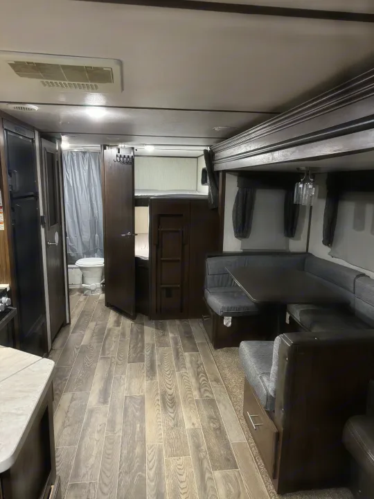 Inside an RV rental, showing the dinette, bunk beds, kitchen area, and bathroom with toilet/shower. Wood-look flooring.. Forest River Cherokee Alpha Wolf 2018